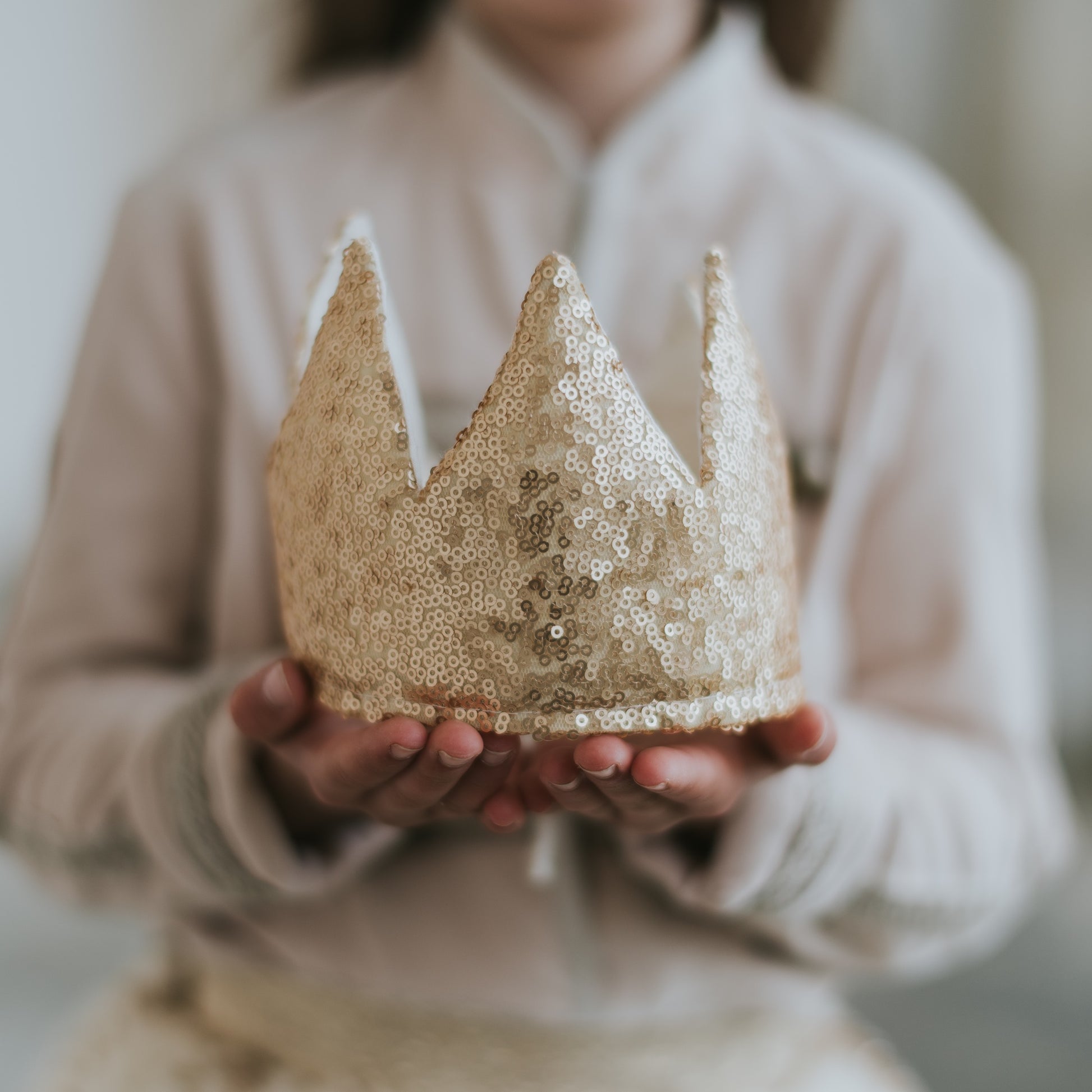 Person holding a FableHeart matte gold sequin crown for children, showcasing the intricate details and craftsmanship of the adjustable accessory.